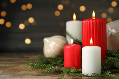Burning candles and festive decor on wooden table against blurred Christmas lights, space for text