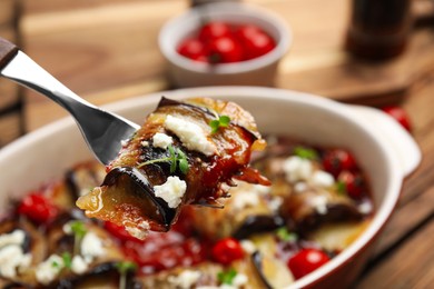 Fork with tasty eggplant roll over baking dish, closeup