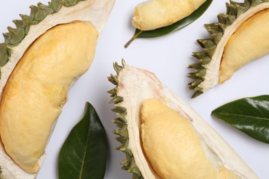 Pieces of fresh ripe durian and leaves on white background, flat lay