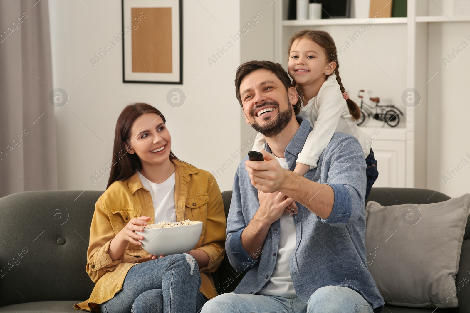 Photo of Happy family watching movie at home. Father changing TV channels with remote control