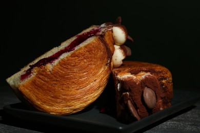 Photo of Round croissant with jam, cream and chocolate chips on grey table, closeup. Tasty puff pastry