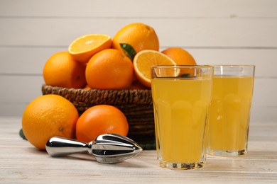 Photo of Many ripe juicy oranges, squeezer and fresh juice on white wooden table