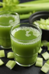Photo of Glasses of delicious celery juice and vegetables on black table, closeup