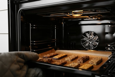 Woman taking delicious healthy granola bars from oven, closeup