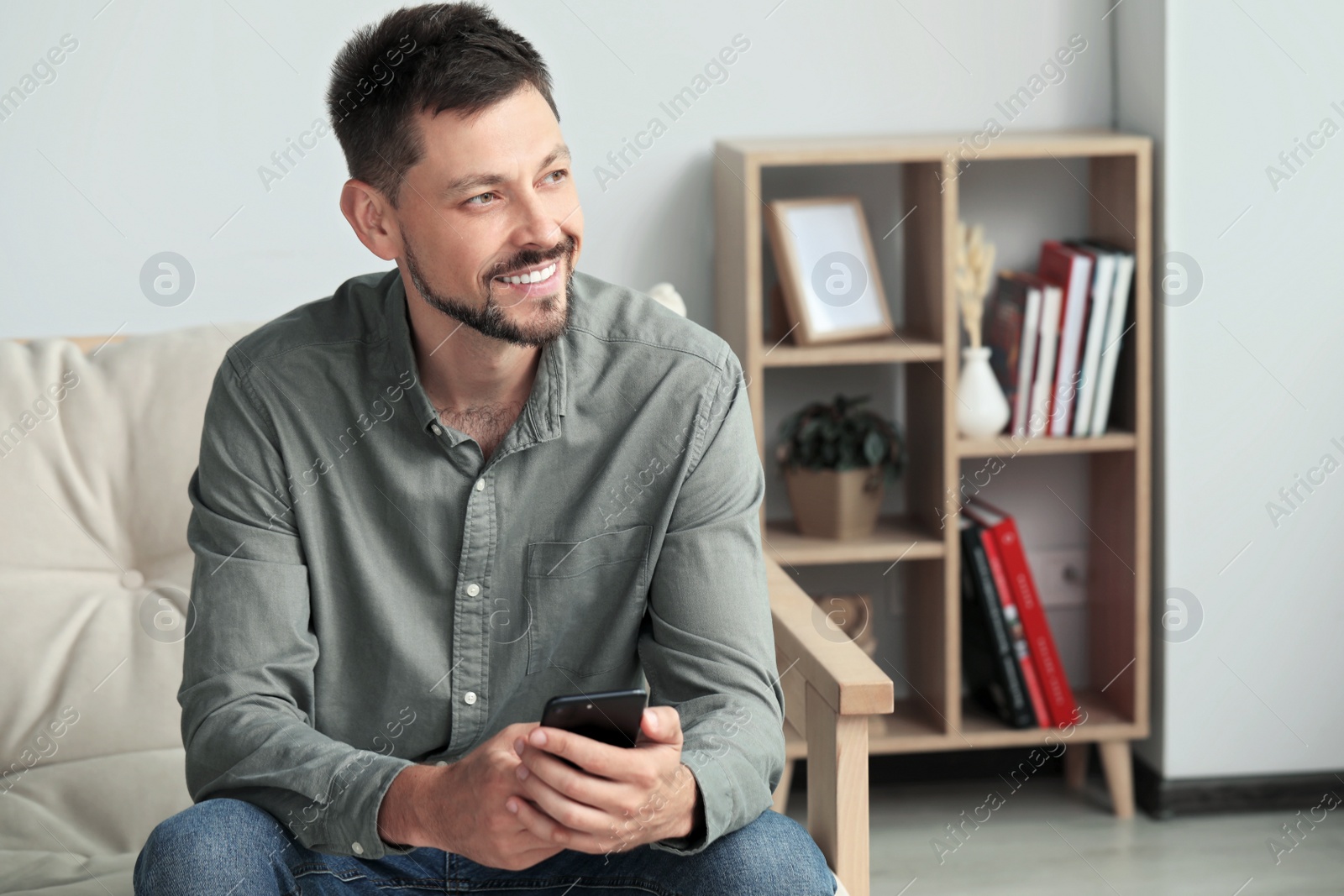 Photo of Happy handsome man using smartphone at home