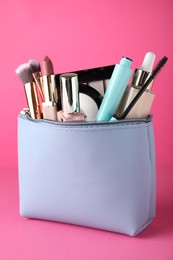 Cosmetic bag with makeup products and accessories on pink background