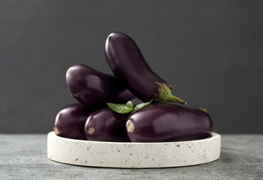Photo of Ripe purple eggplants and basil on grey table, closeup