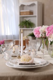 Stylish table setting with beautiful peonies and burning candles indoors