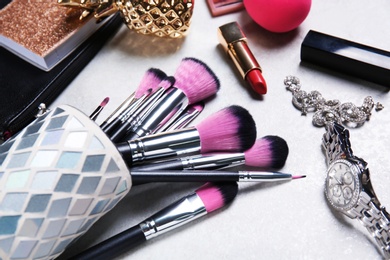 Photo of Holder with professional brushes, makeup products and accessories on light background