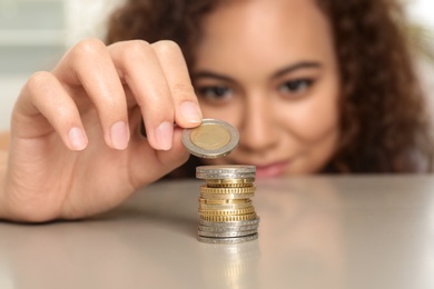Young African-American woman stacking coins at table, focus on hand