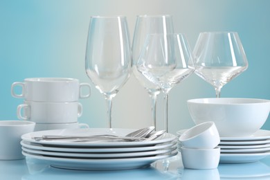 Photo of Set of many clean dishware, cutlery and glasses on light blue table