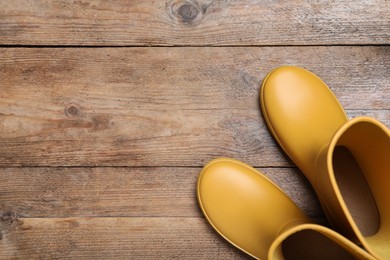 Photo of Yellow rubber boots on wooden background, top view. Space for text