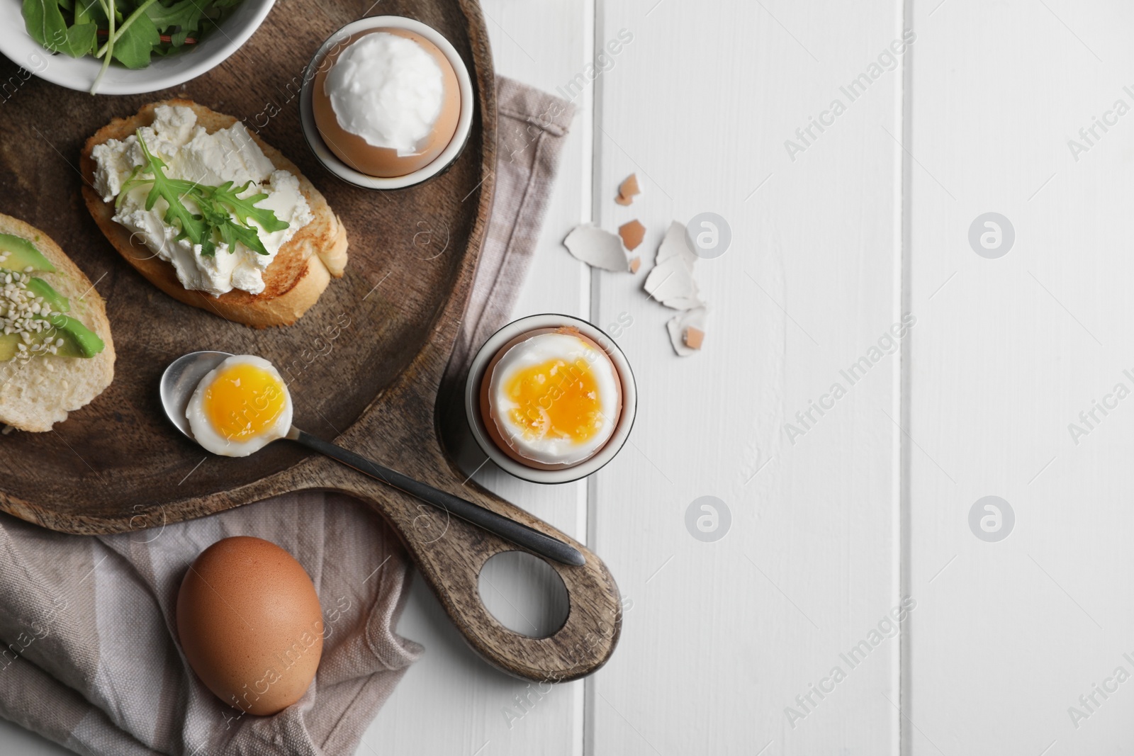 Photo of Breakfast with soft boiled eggs served on white wooden table, flat lay. Space for text