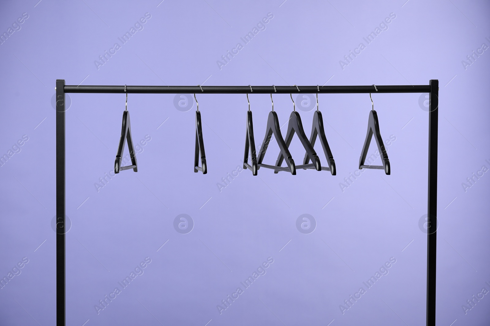 Photo of Black clothes hangers on rack against purple background