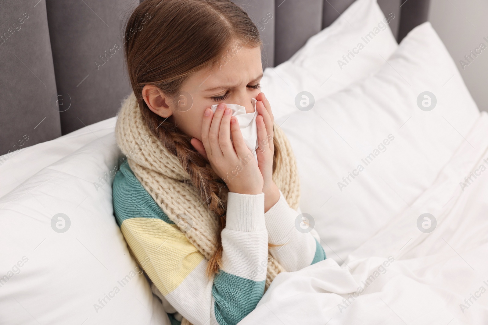 Photo of Sick girl with tissue coughing on bed at home