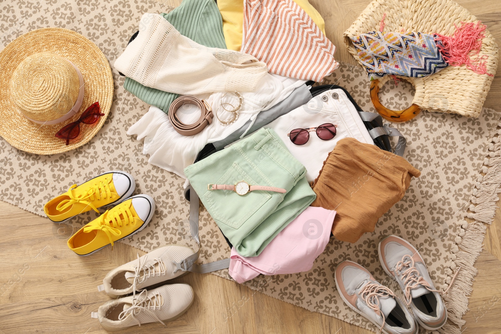 Photo of Open suitcase full of clothes and summer accessories near shoes on floor, top view