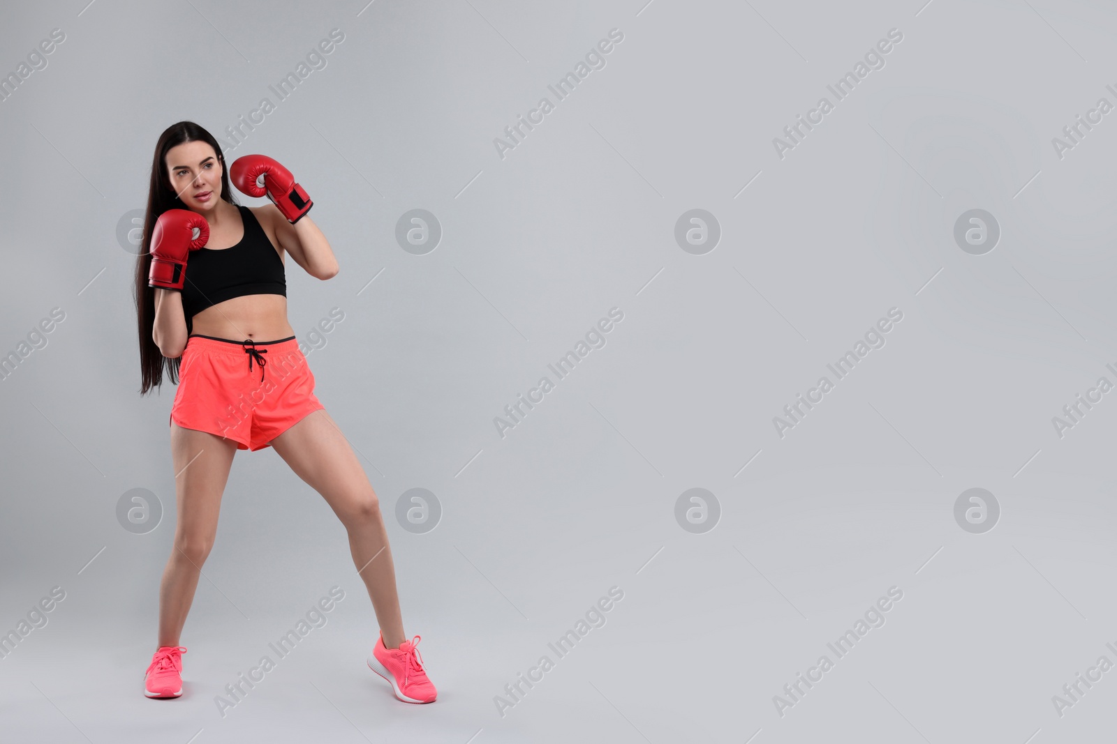 Photo of Beautiful woman in boxing gloves training on grey background. Space for text