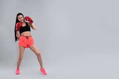 Beautiful woman in boxing gloves training on grey background. Space for text