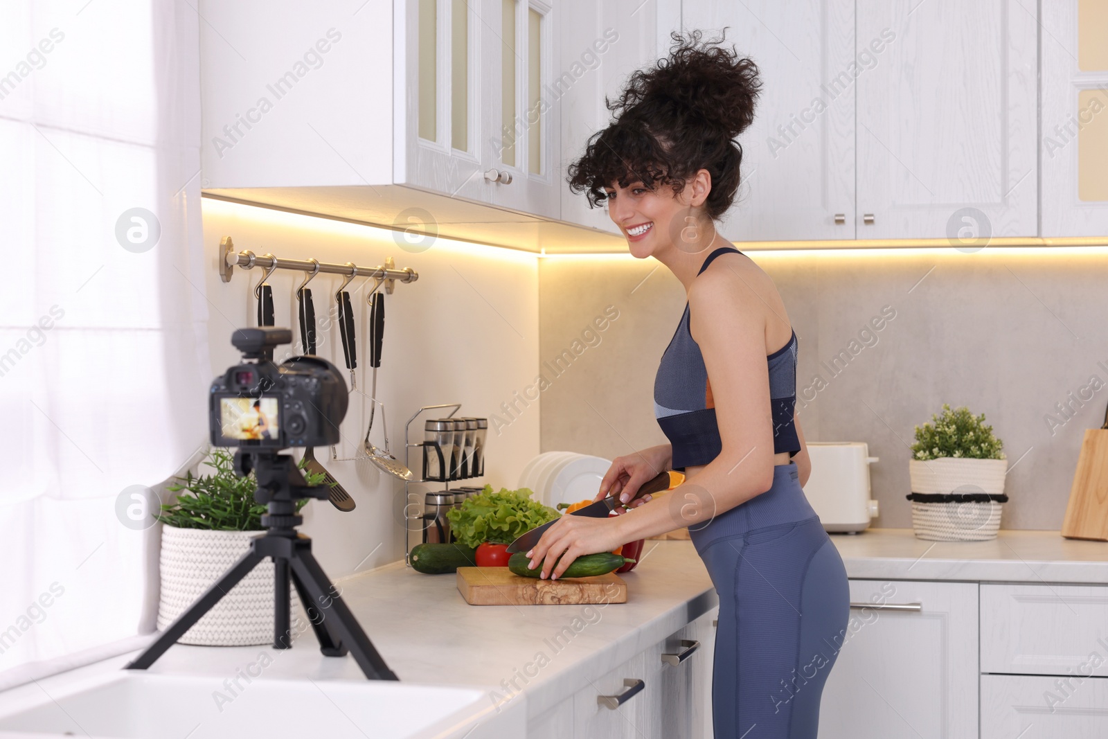 Photo of Smiling food blogger cooking while recording video in kitchen