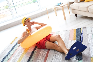 Photo of Shirtless man with inflatable ring and bottle of drink wearing flippers on floor at home
