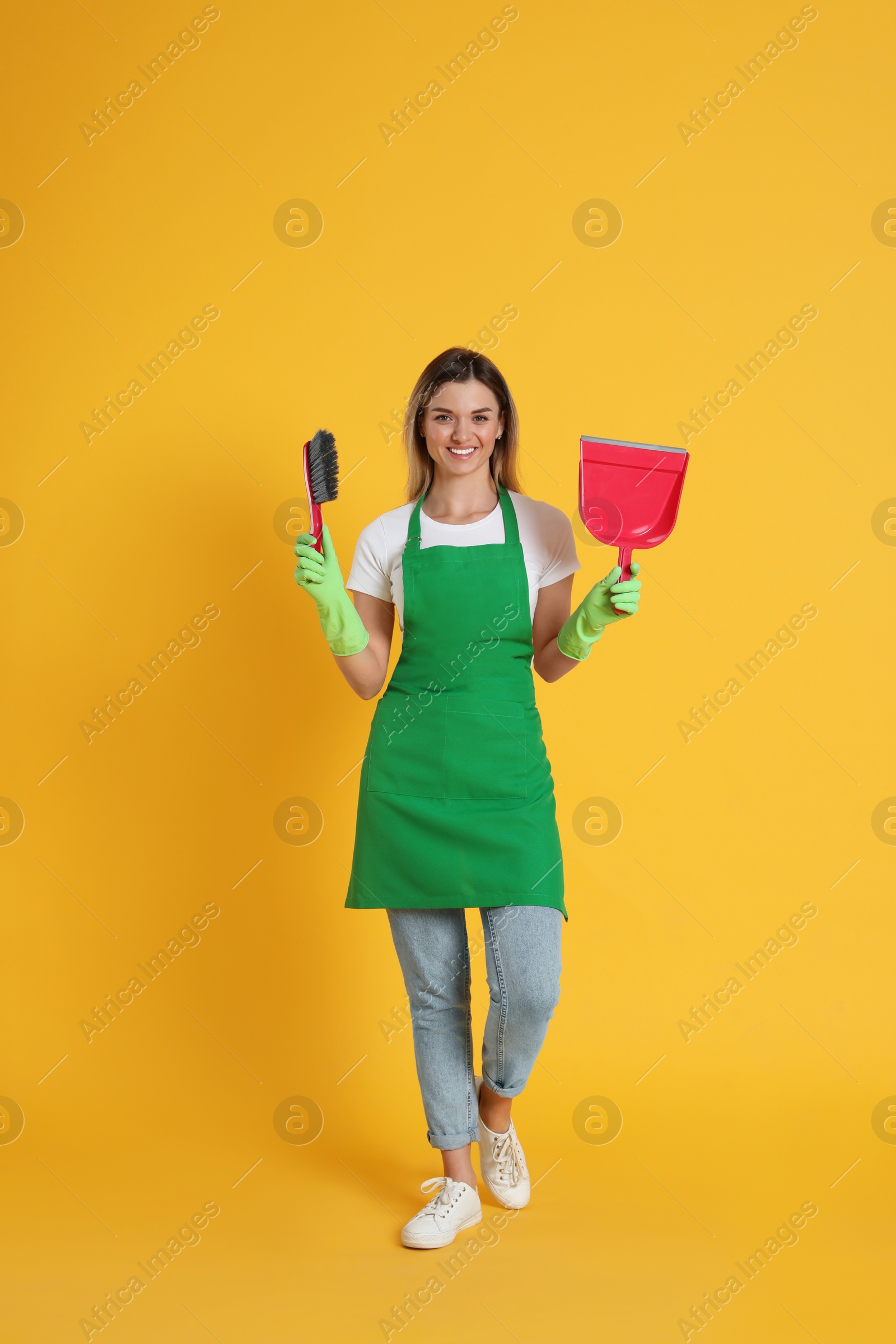 Photo of Young woman with broom and dustpan on orange background