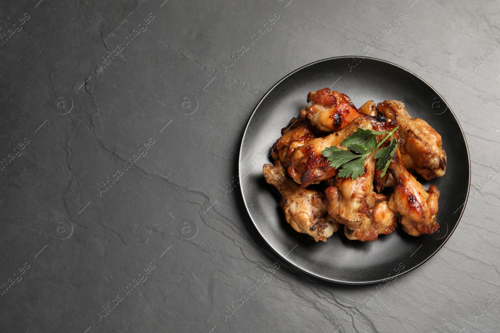 Photo of Plate with delicious fried chicken wings on black table, top view. Space for text