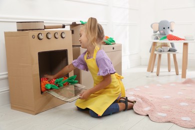 Little girl playing with toy cardboard oven at home