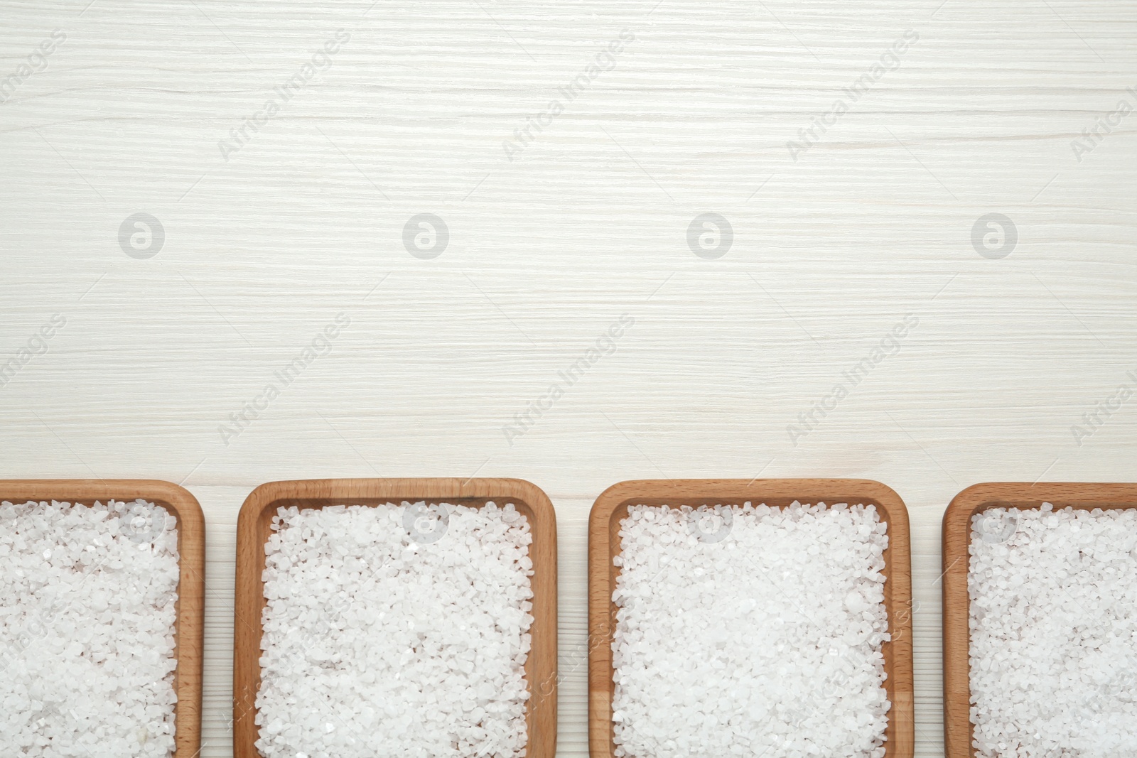 Photo of Plates with natural sea salt on white wooden table, flat lay. Space for text