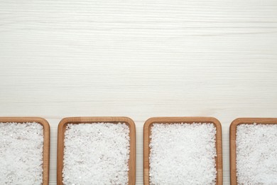 Plates with natural sea salt on white wooden table, flat lay. Space for text