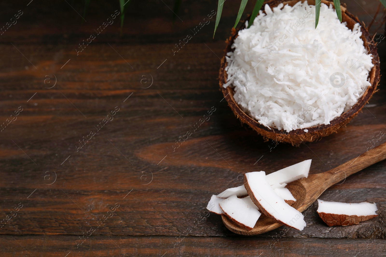 Photo of Coconut flakes, spoon and nut on wooden table, space for text