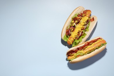 Delicious hot dogs with bacon, lettuce, onion and pickle on light blue background, flat lay. Space for text