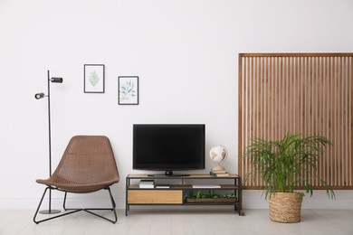 Photo of Elegant room interior with modern TV on cabinet, chair and beautiful houseplants