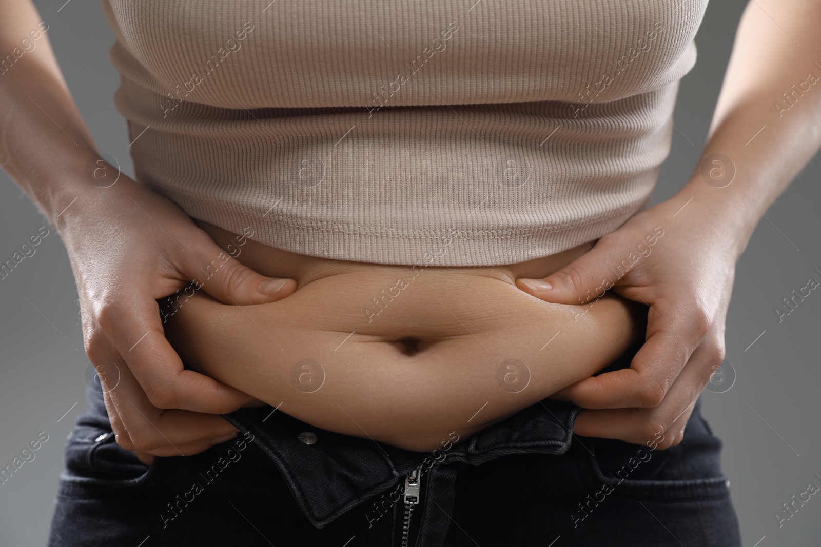 Photo of Woman touching belly fat on grey background, closeup. Overweight problem