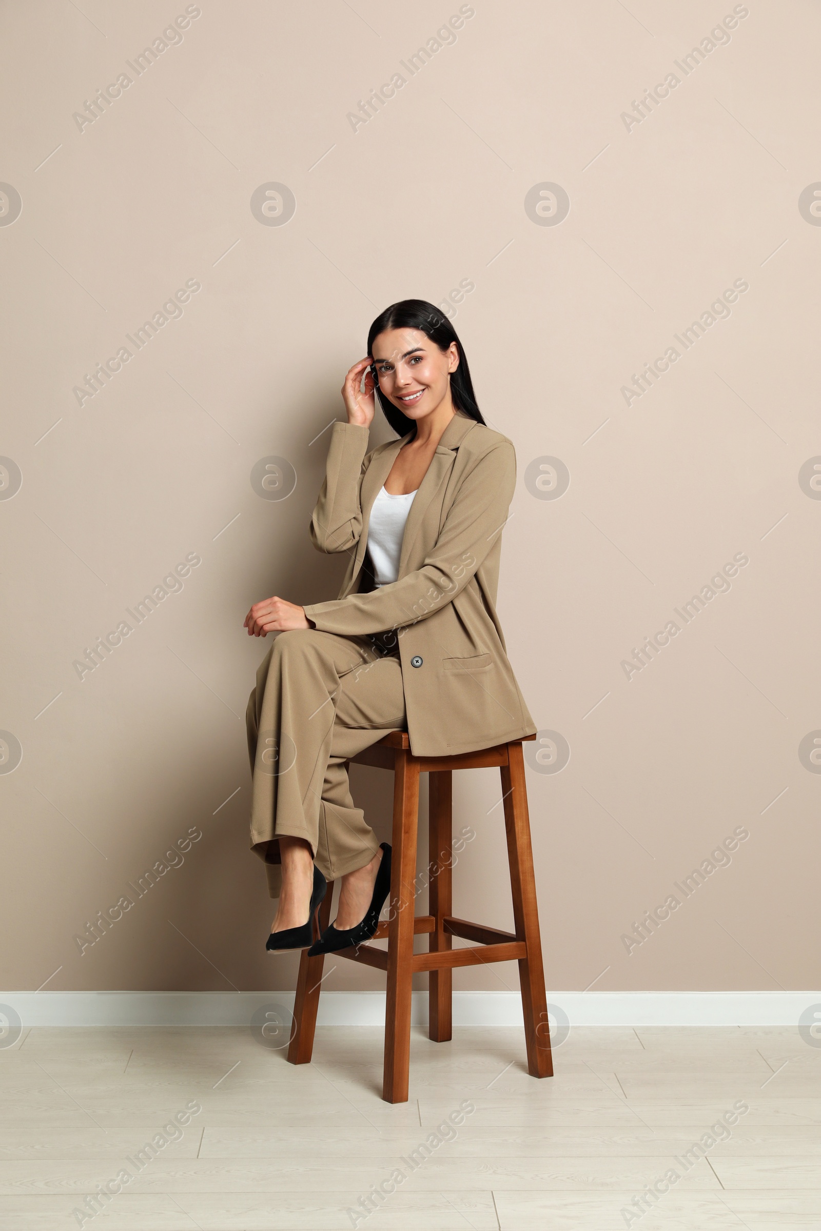 Photo of Beautiful young businesswoman sitting on stool near beige wall