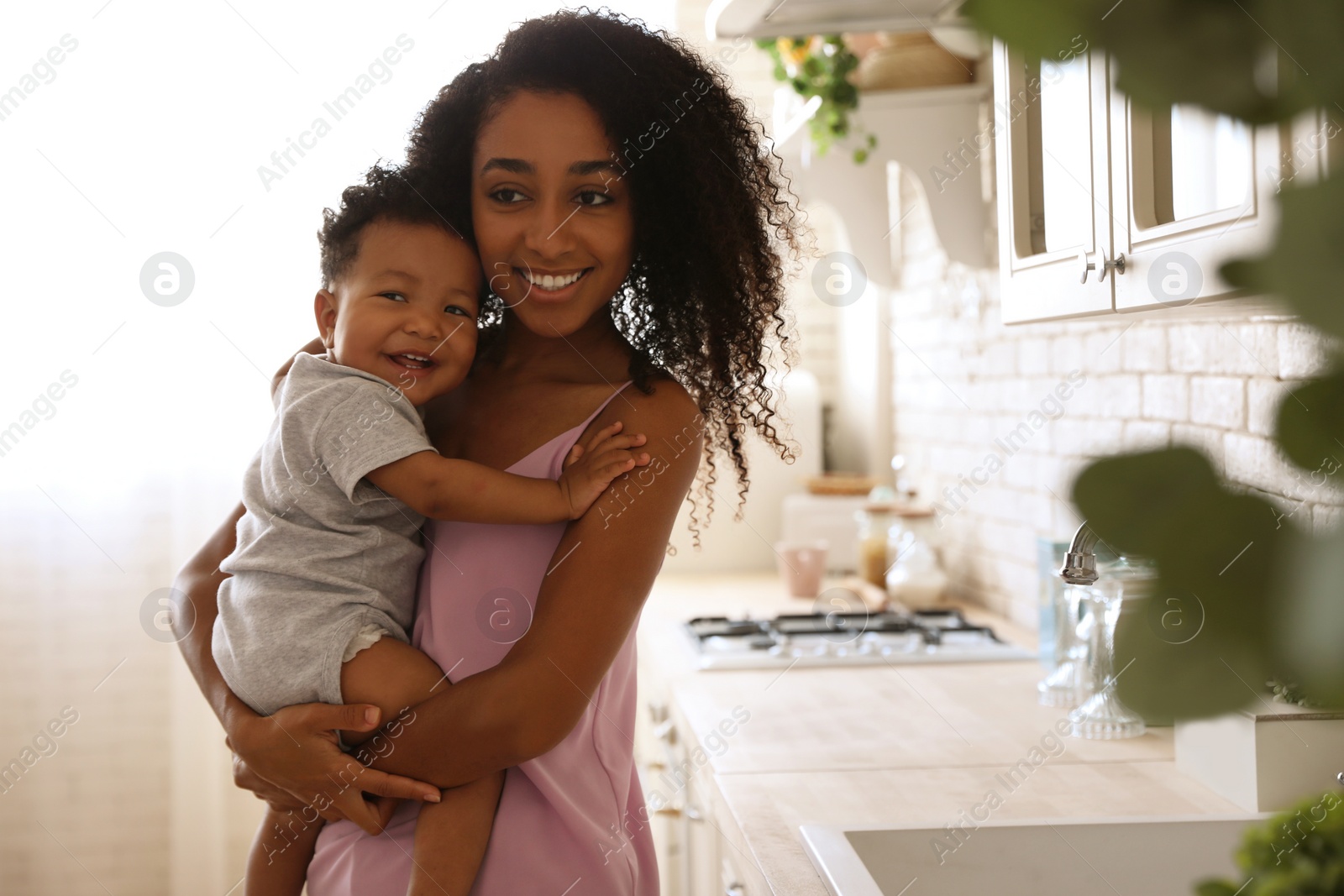 Photo of African-American woman with her baby in kitchen. Happiness of motherhood