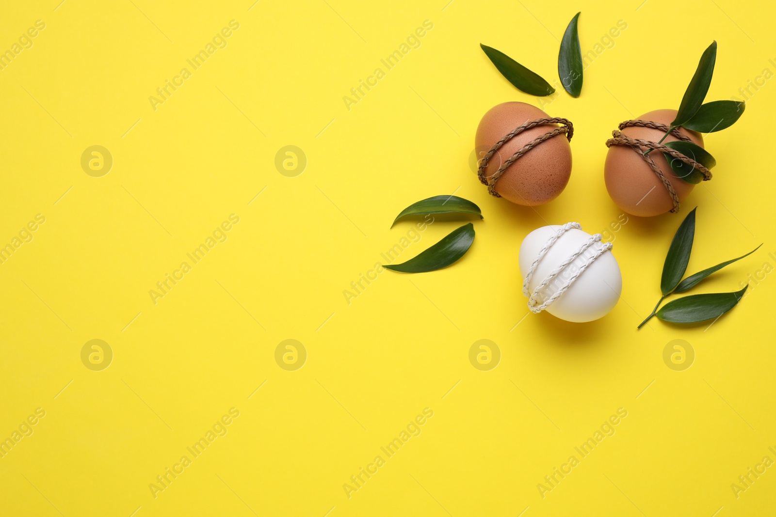 Photo of Easter eggs decorated with green leaves on yellow background, flat lay. Space for text