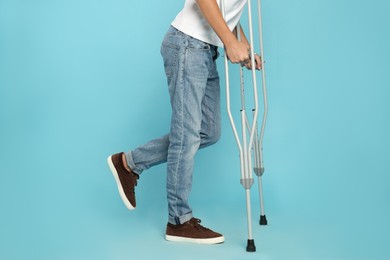 Photo of Man with injured leg using crutches on turquoise background, closeup