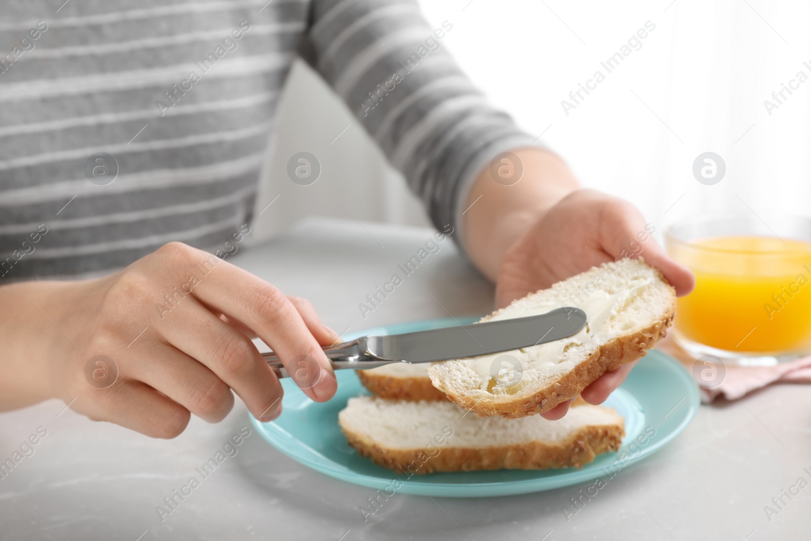 Photo of Woman spreading butter on slice of bread over table, closeup