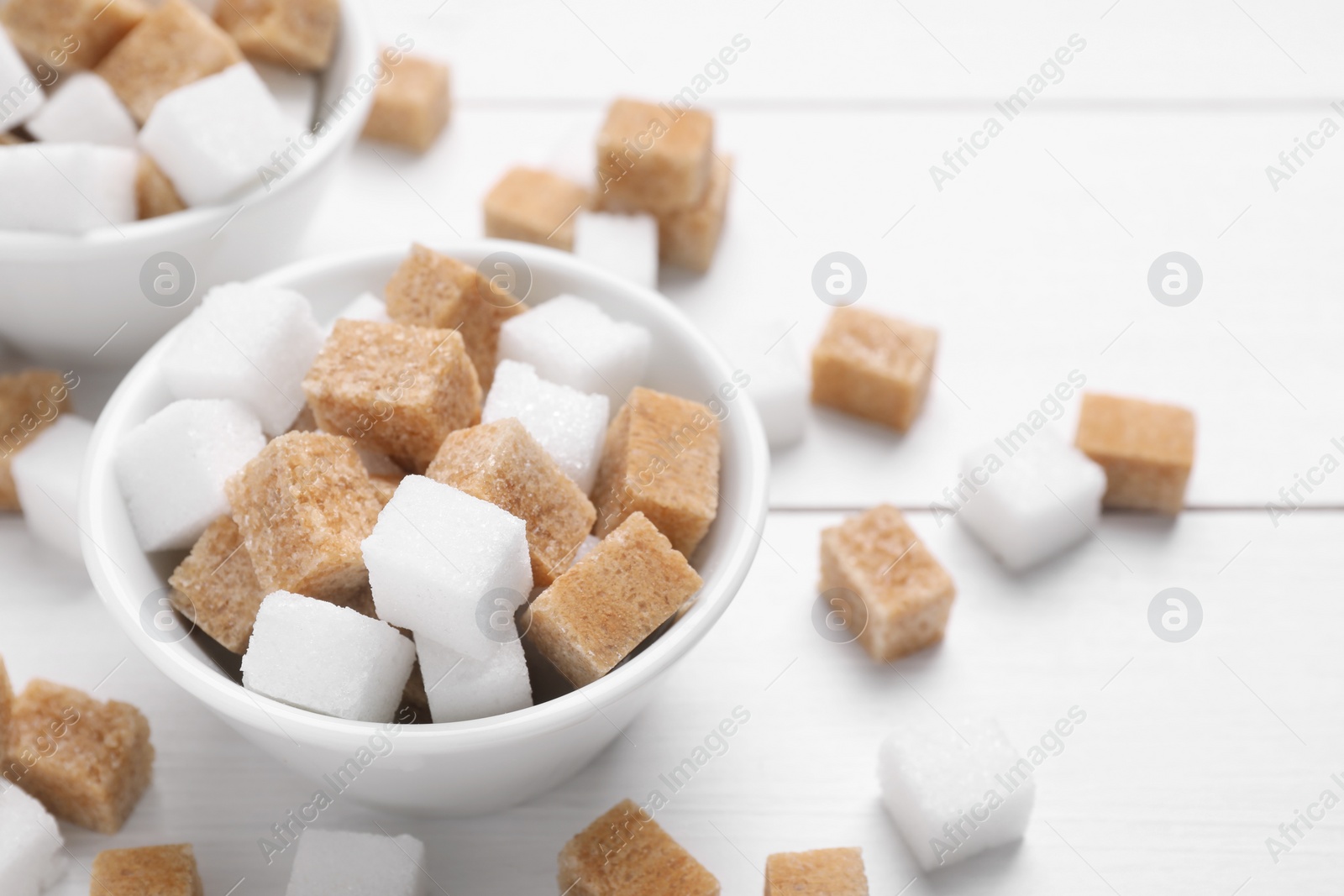 Photo of Different sugar cubes in bowls on white table, closeup