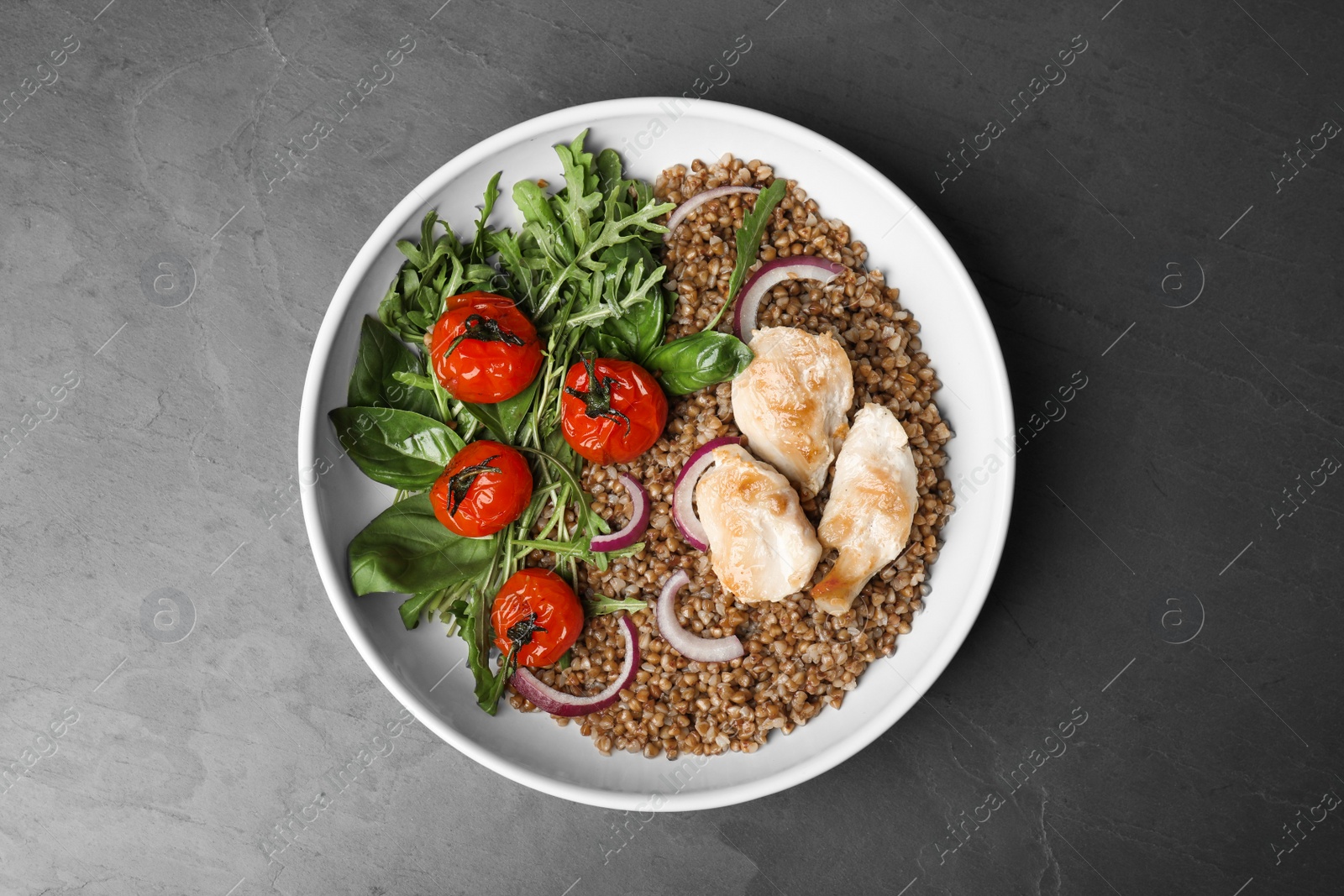 Photo of Tasty buckwheat porridge with meat and vegetables on grey table, top view