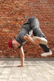 Man dancing hip hop near brick wall outdoors, low angle view