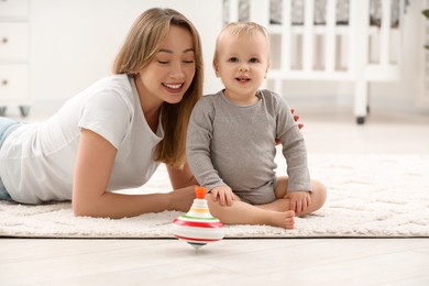 Children toys. Happy mother with her little son and spinning top on rug at home