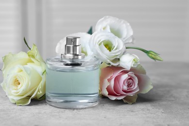 Photo of Bottle of perfume and flowers on grey table indoors