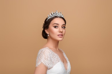 Beautiful young woman wearing luxurious tiara on beige background