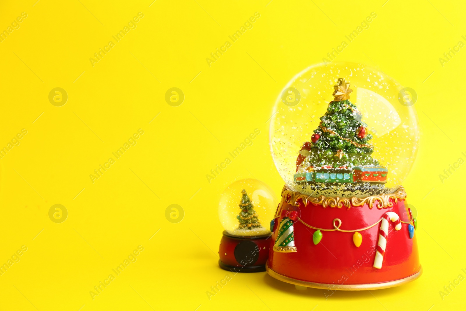 Photo of Beautiful snow globes with Christmas trees on yellow background, space for text