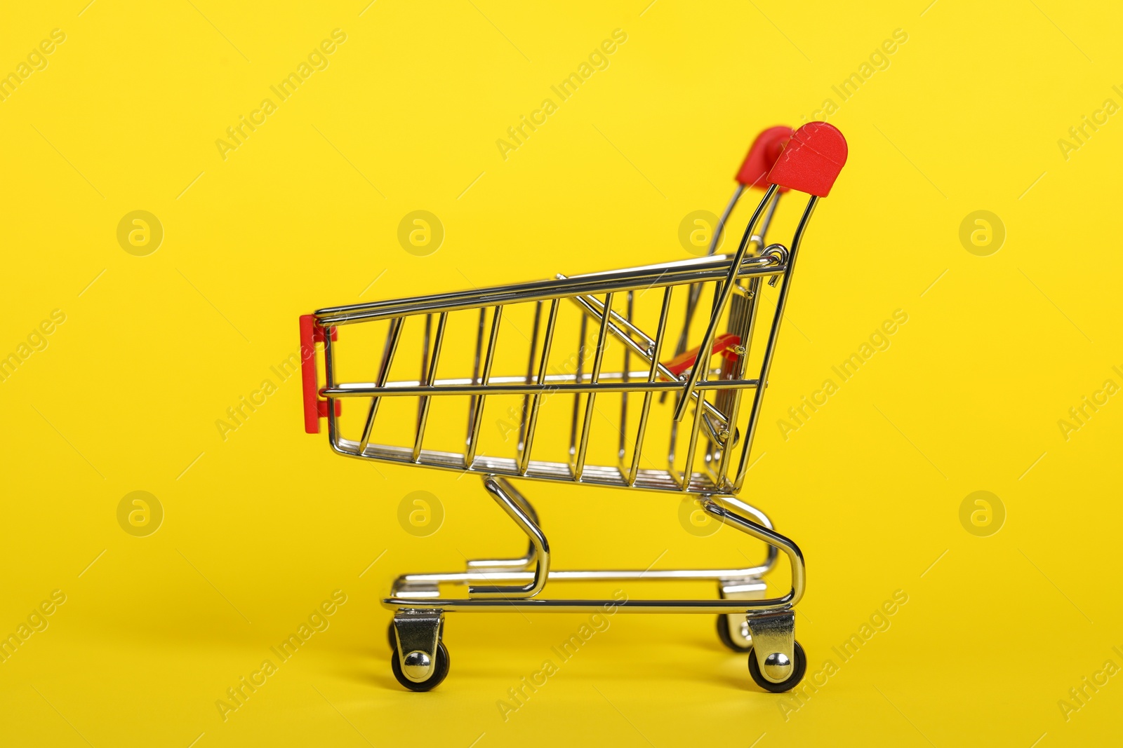 Photo of Small metal shopping cart on yellow background