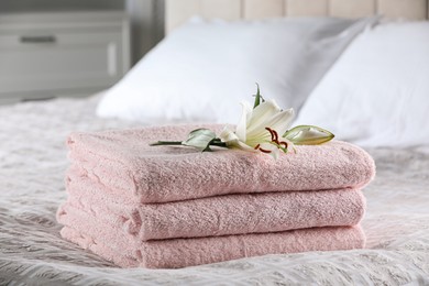 Photo of Stack of clean towels and flower on bed indoors