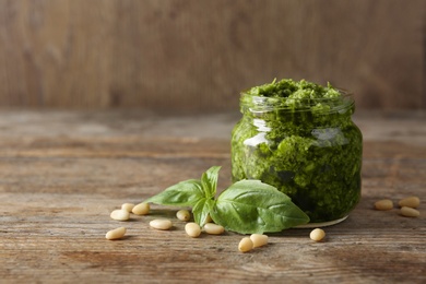 Photo of Jar of pesto sauce with basil leaves and pine nuts on wooden table. Space for text