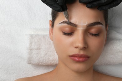 Photo of Beautician making permanent eyebrow makeup to young woman, top view. Space for text