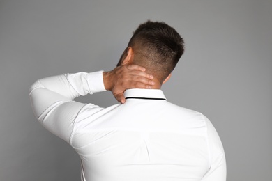 Businessman suffering from neck pain on light grey background